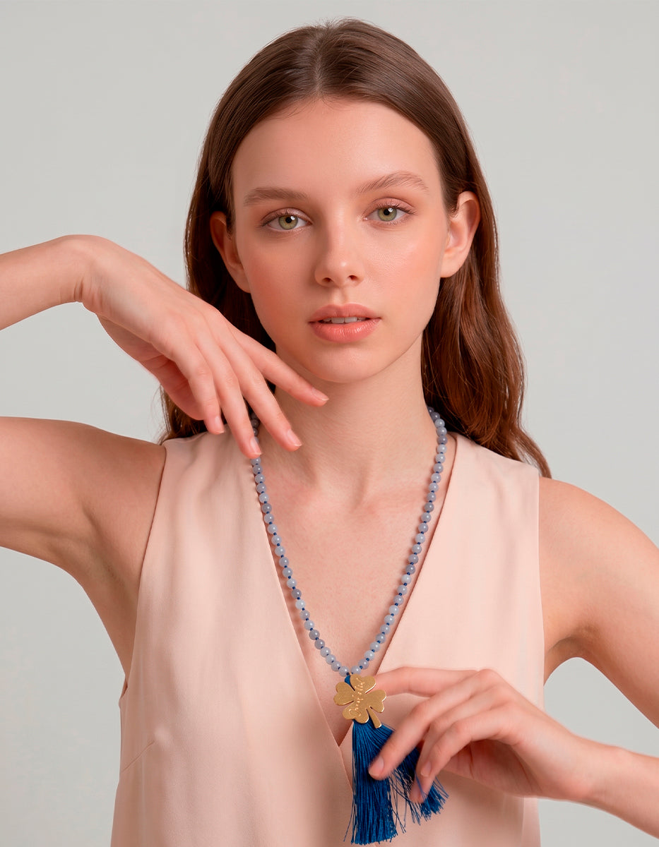 Collar de cuentas azul con dije trébol en bronce baño oro de 22kt y pompon