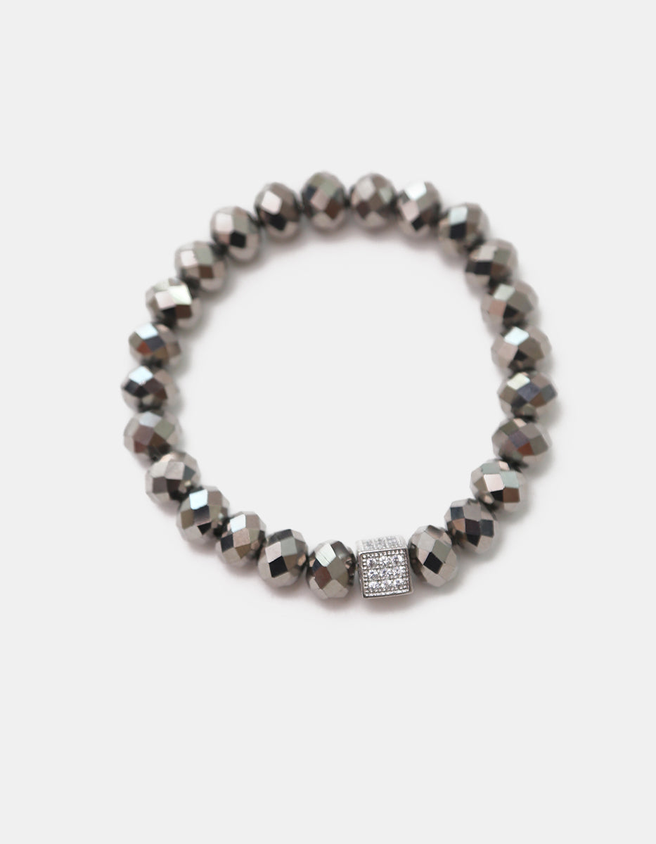 Pulsera de cristal gris metálico con dije cúbico en bronce con baño de platino y circonias