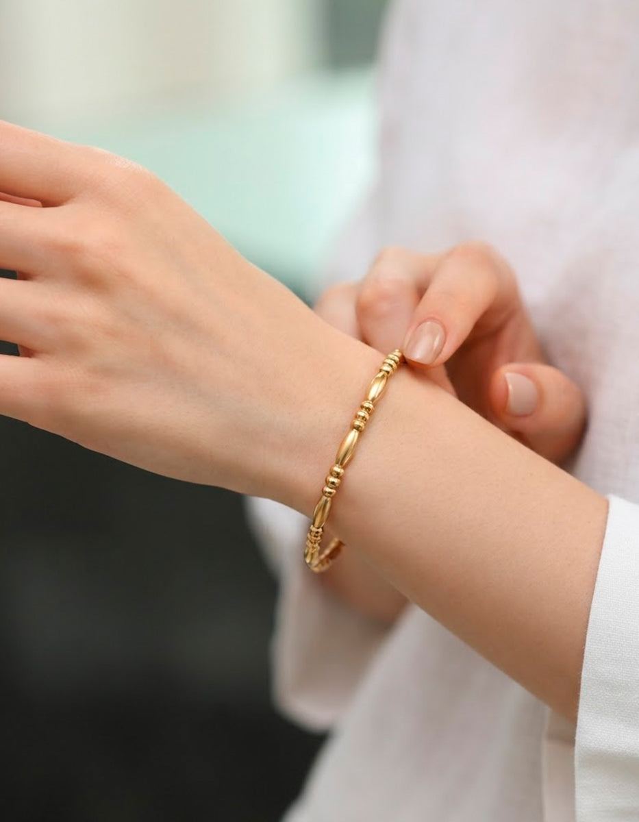 Brazalete rígido de bronce en baño de oro 22 kt con secuencia de balines y secciones de oliva