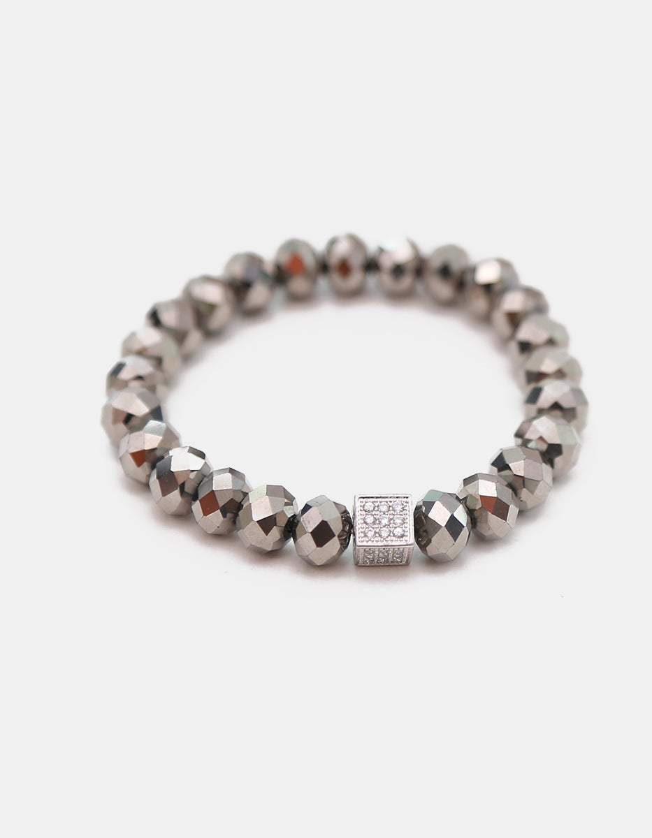 Pulsera de cristal gris metálico con dije cúbico en bronce con baño de platino y circonias