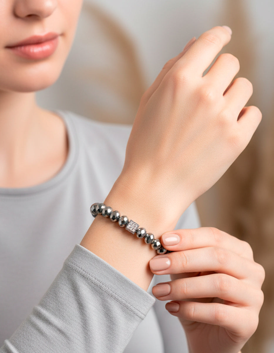 Pulsera de cristal gris metálico con dije cúbico en bronce con baño de platino y circonias