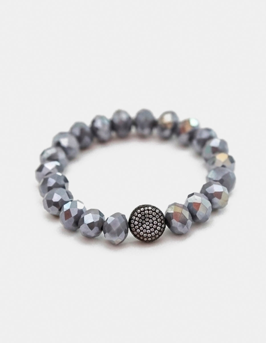 Pulsera de cristal gris metálico con dije esférico en bronce con baño de rutenio y circonias